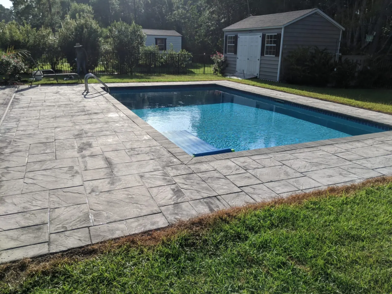 A rectangular swimming pool with a wide grey stamped concrete deck wrapping all four sides